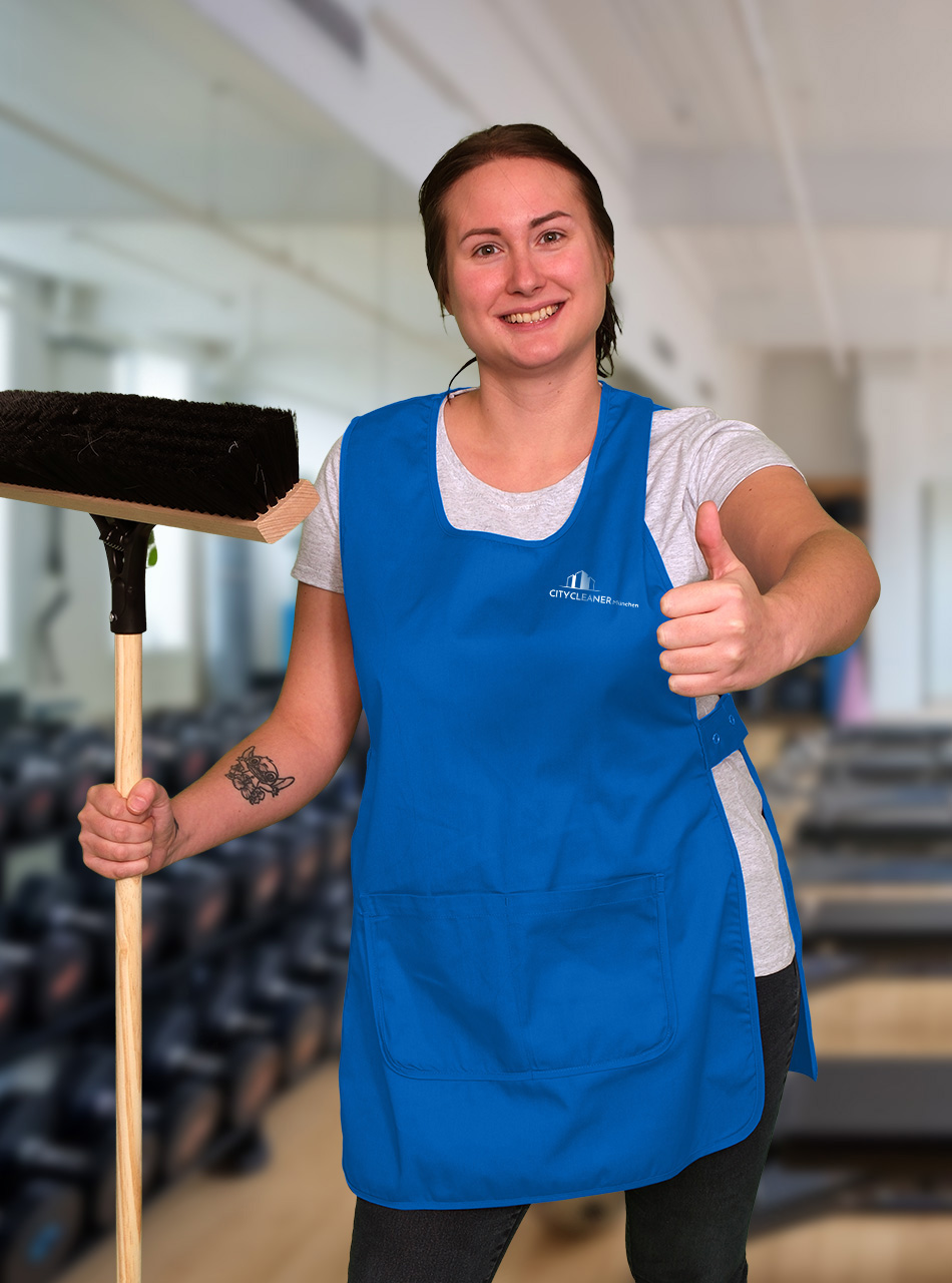 Eine Mitarbeiterin der Fitnesscenter-Reinigung München mit blauer Weste, Besen und Daumen noch